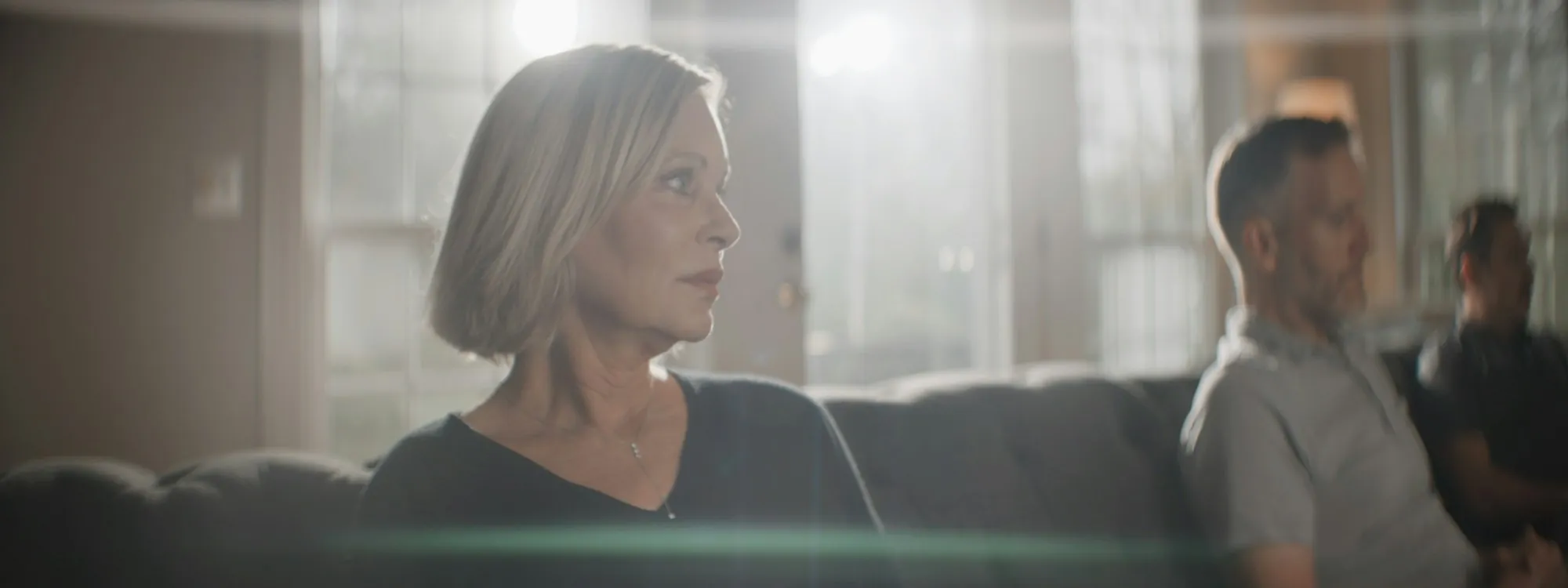 A woman and an older man talking on a sofa in a sunlit room