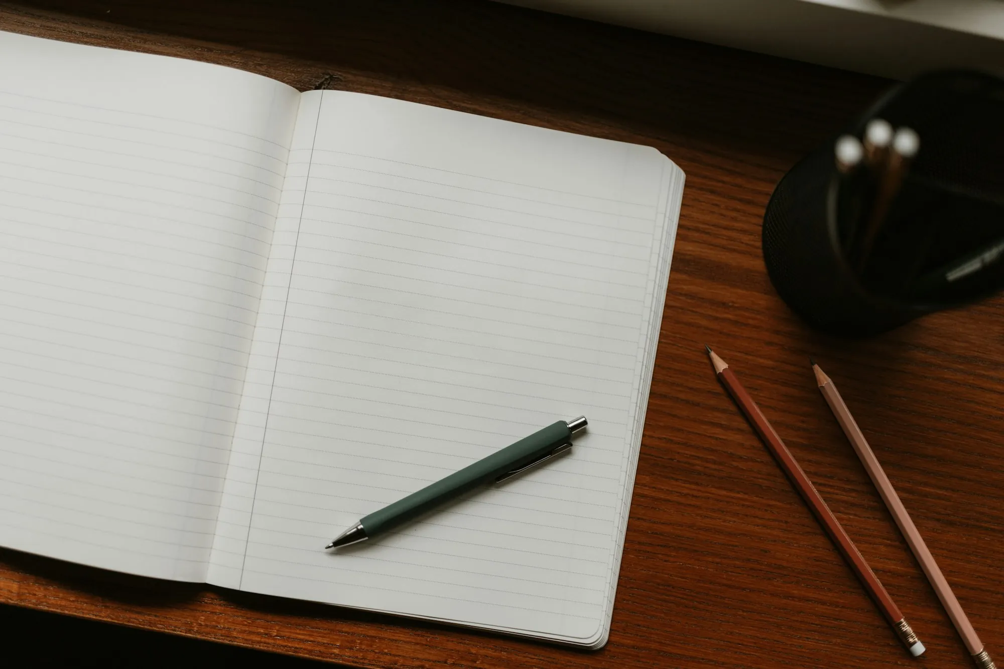 An open notebook with a pen and pencils on a desk