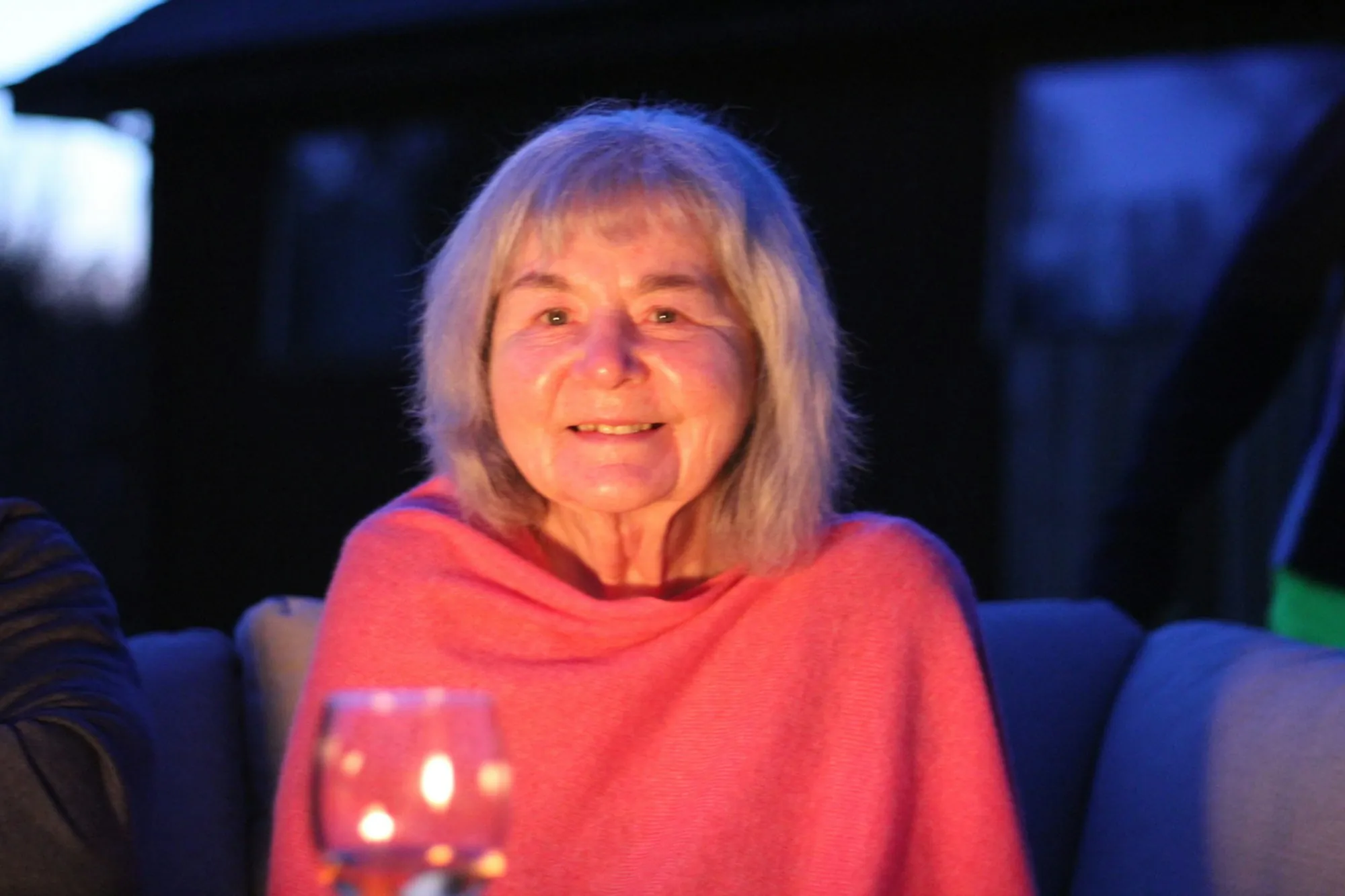 An older woman smiling, wrapped in a soft shawl